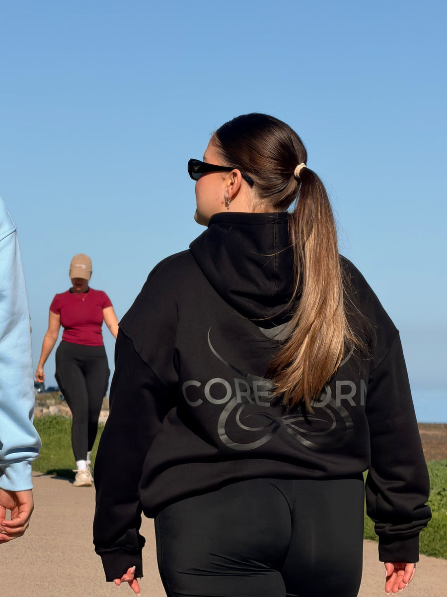 Back print of the black CORE O.G. Hoodie by the beach