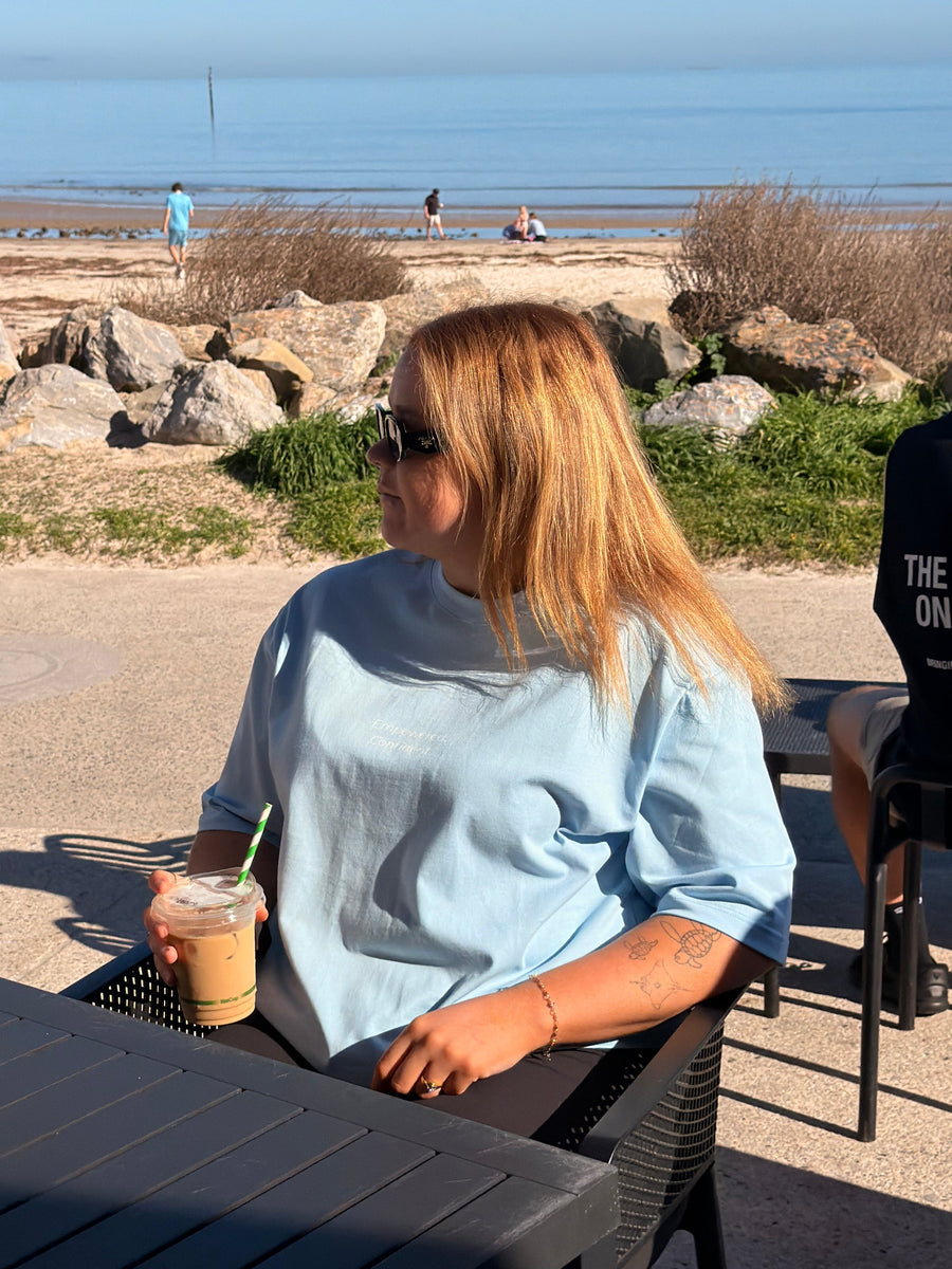 Woman in the Alpine Sky Empowered Oversized Tee at a beachside café